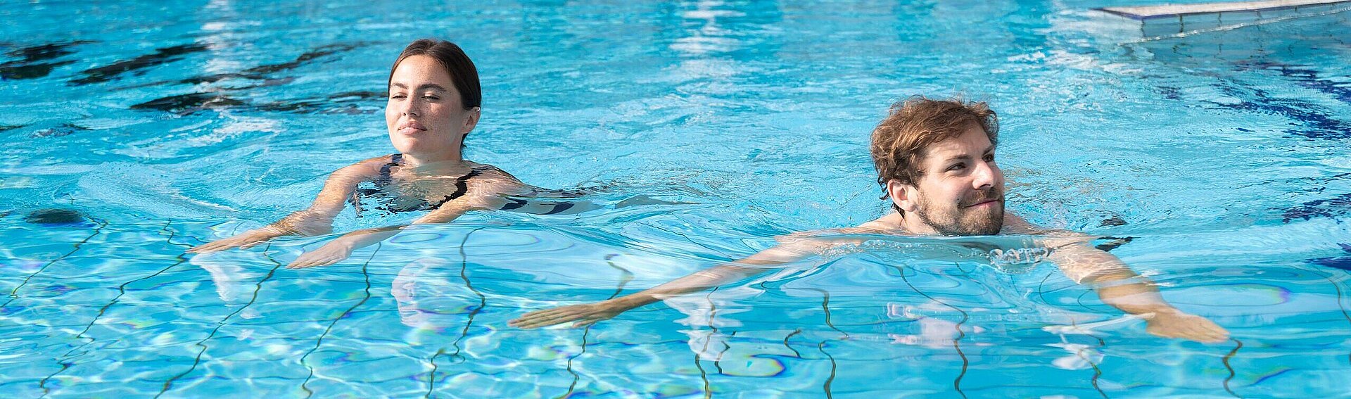 Pärchen schwimmt im Pool vom Thermenhotel Vier Jahreszeiten Swimming through the outdoor pool of the Thermenresort Loipersdorf